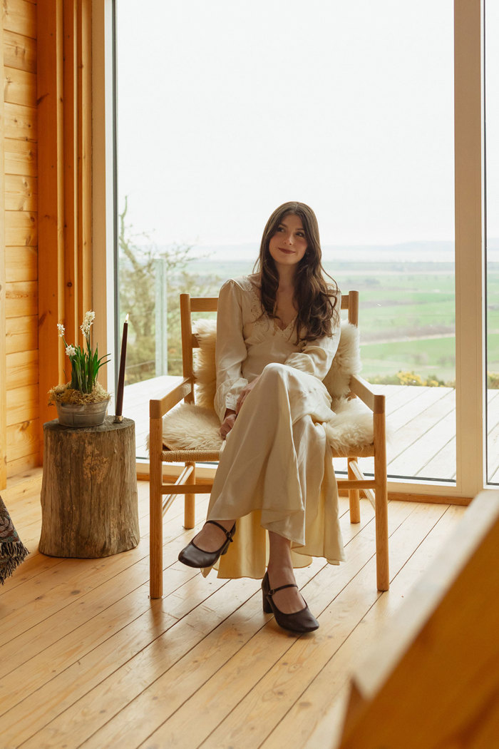 bride sits smiling on wooden chair indoors at guardswell farm