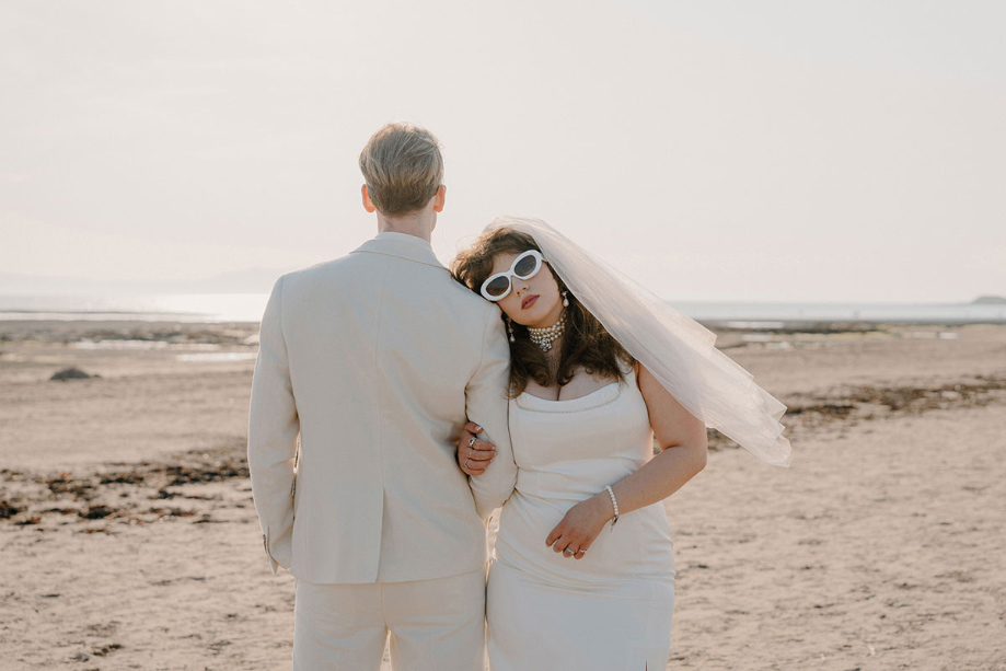 Bride leans on groom's shoulder on troon beach