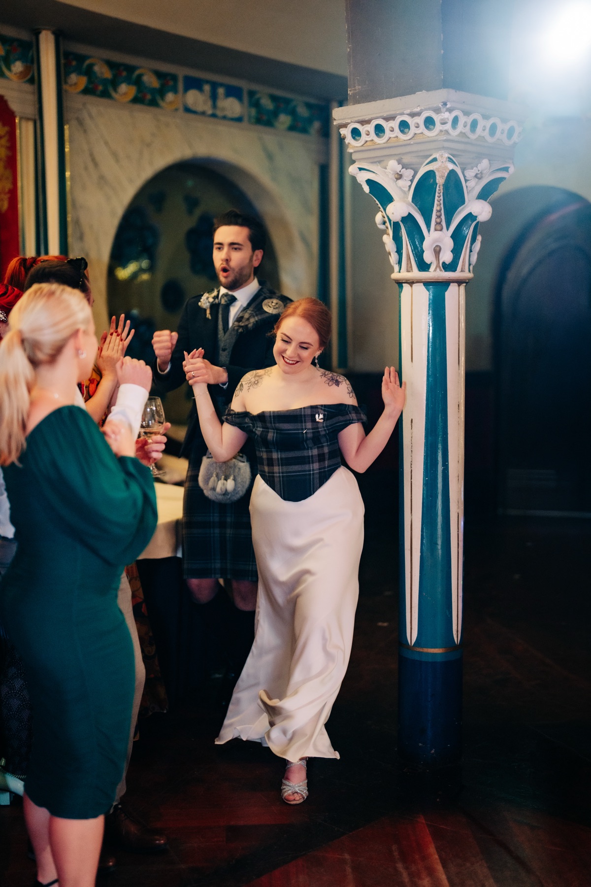 Robyn and James enter their evening wedding reception at Òran Mór in Glasgow, with Robyn wearing a bespoke tartan corset matching James's kilt.