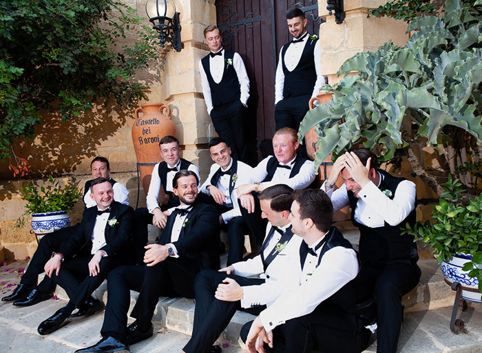 a group of jovial men wearing suits sitting on a set of stone steps in front of a large wooden door and stone building