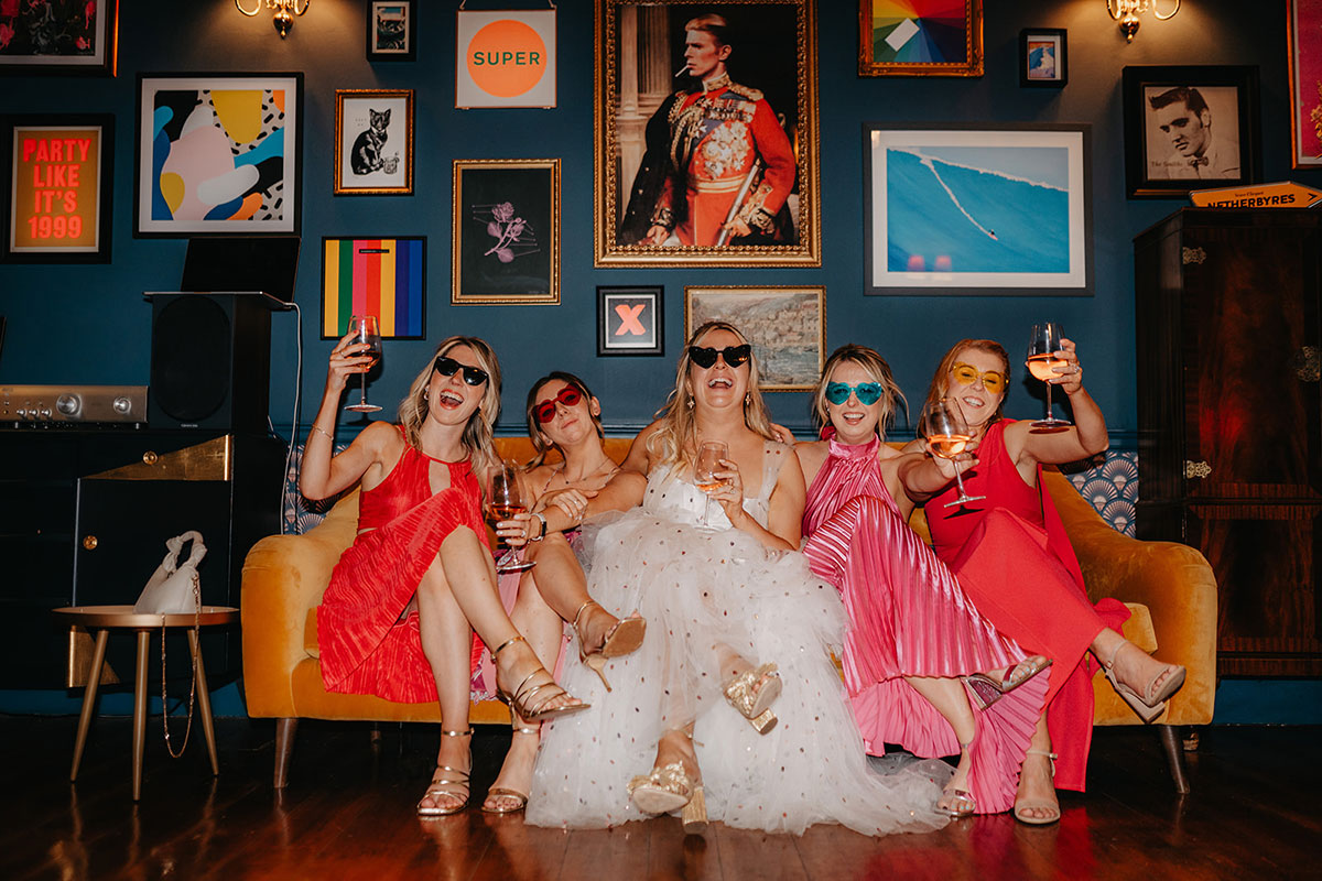 Bride and wedding guests relaxing in the colourful Lounge at Netherbyres House with eclectic artwork and interiors.