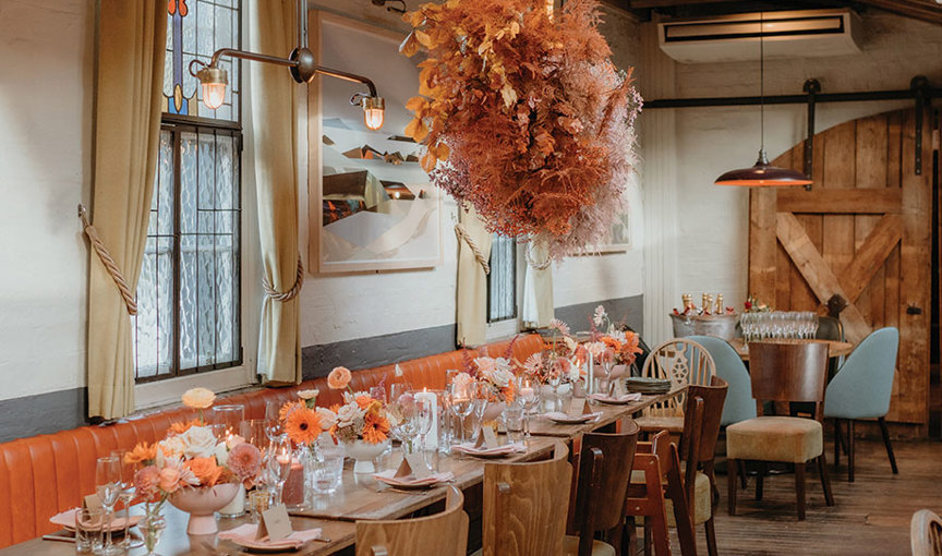 a long table at Ubiquitous Chip with flowers and glasses on it and coral dried flower 'flower bomb' hanging over it