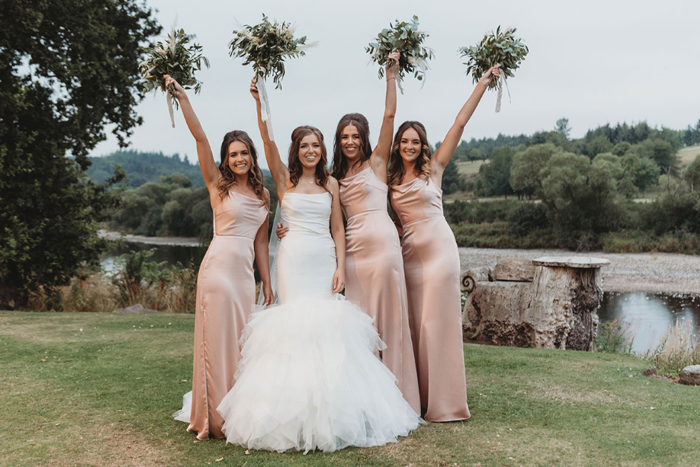 Bride and three bridesmaids wearing pink dresses hold bouquets in the air