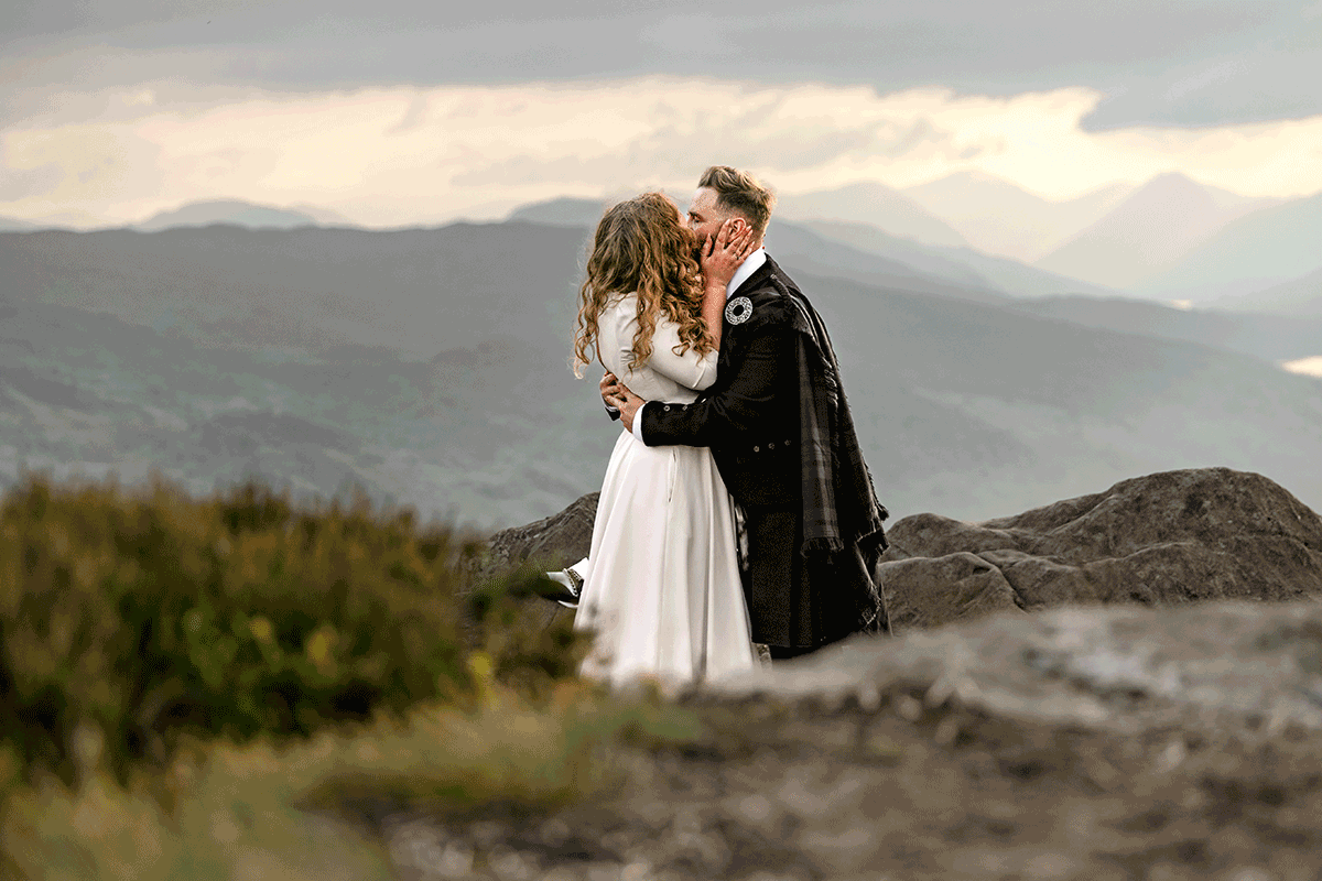 Newlyweds share a kiss following their outdoor Scottish elopement ceremony, surrounded by rugged Highland scenery