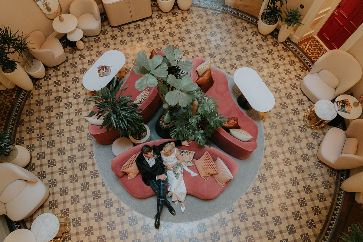 Overhead view of the newlyweds sitting together in a colourful hotel lobby during their Edinburgh wedding