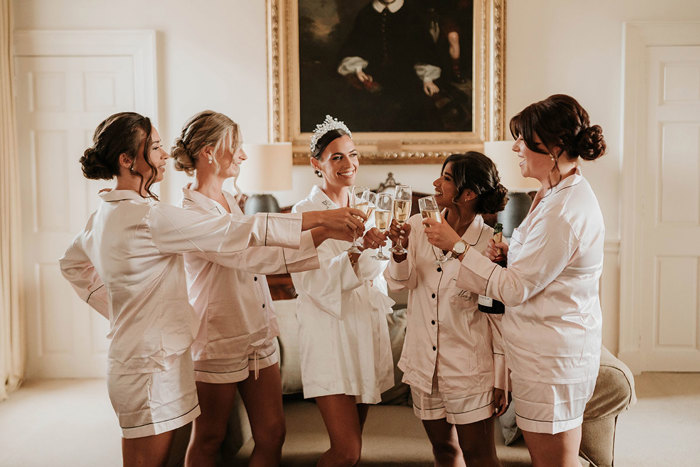 Five women in white pajamas bring their glasses of champagne together in a toast 