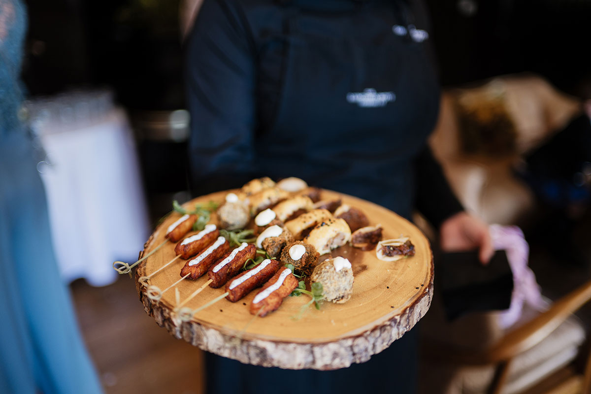 Server holding a rustic wooden board filled with assorted bite-size canapés at a wedding reception