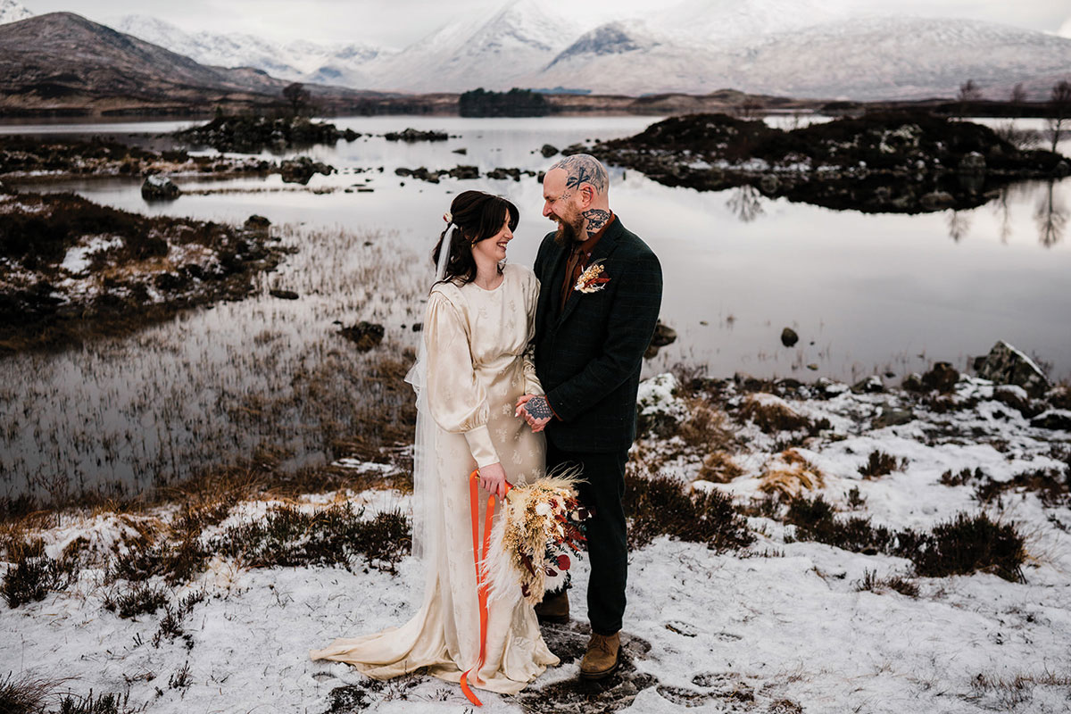 Couple portrait beside a snowy Scottish loch with mountains in the background