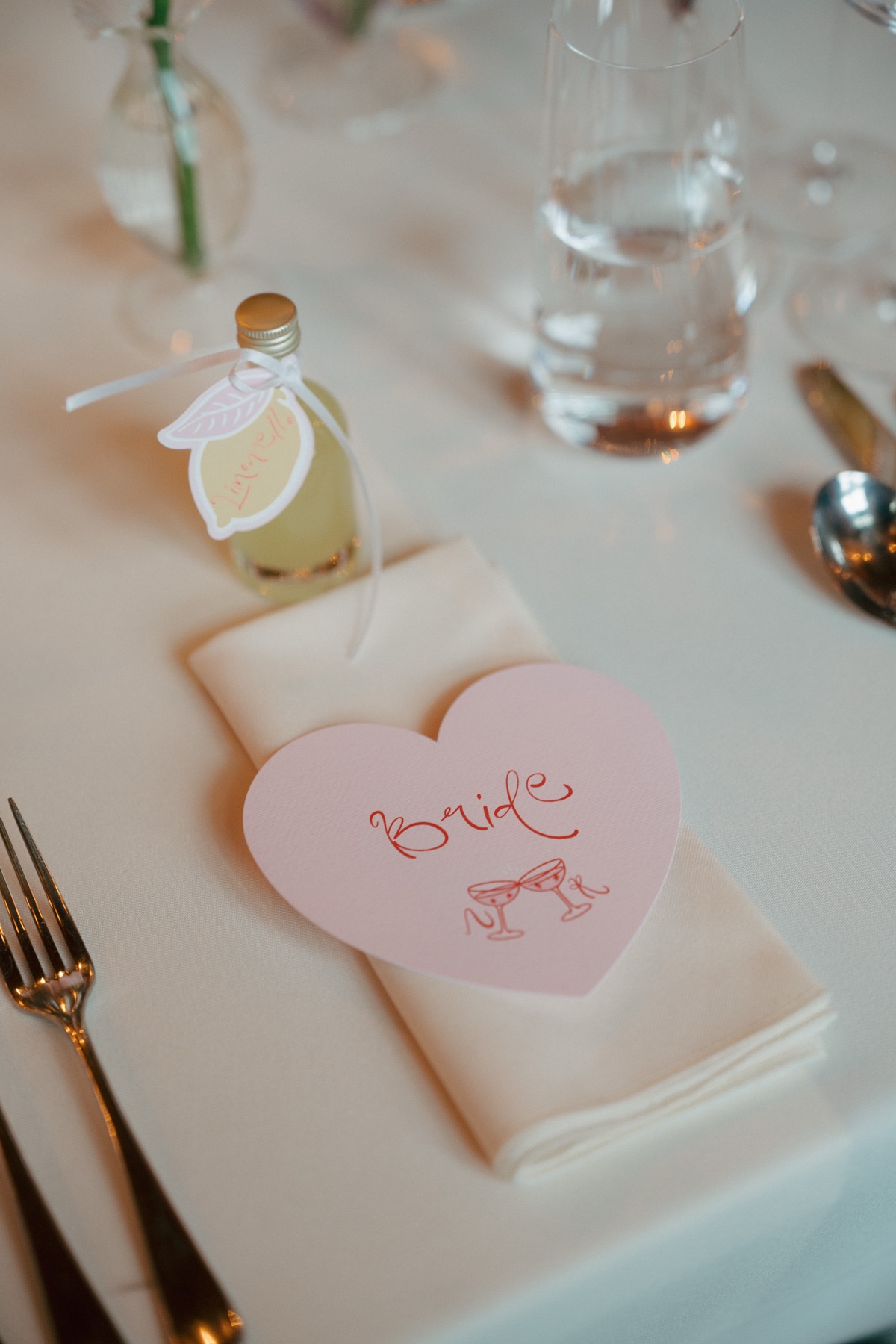 Personalised pink heart-shaped bride place card and miniature limoncello wedding favour on a reception table at Barnbougle Castle.