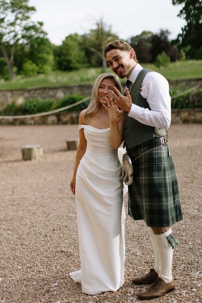 Lia and Louis show their wedding rings while posing in the grounds of Cambo House in Fife.