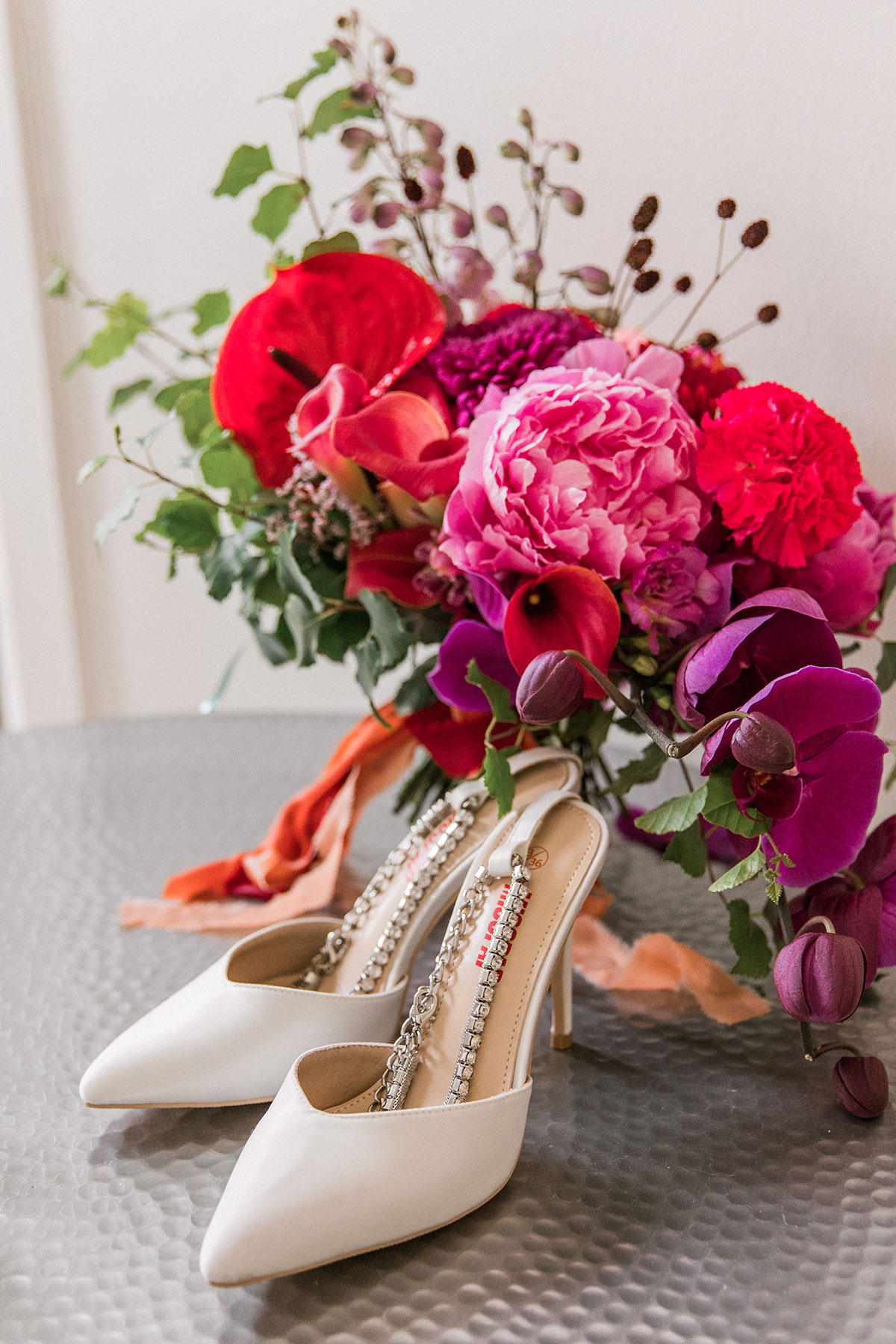 White bridal shoes displayed beside a vibrant pink, purple and red wedding bouquet