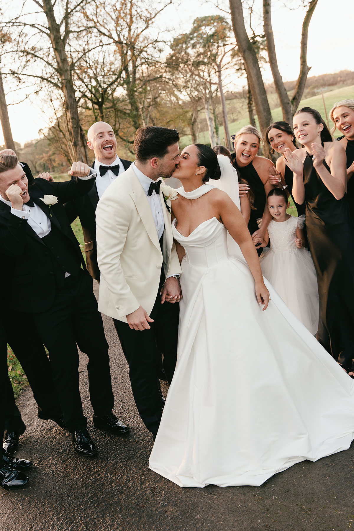 Bride and groom kissing with wedding party celebrating around them at Enterkine Country House wedding in Ayrshire
