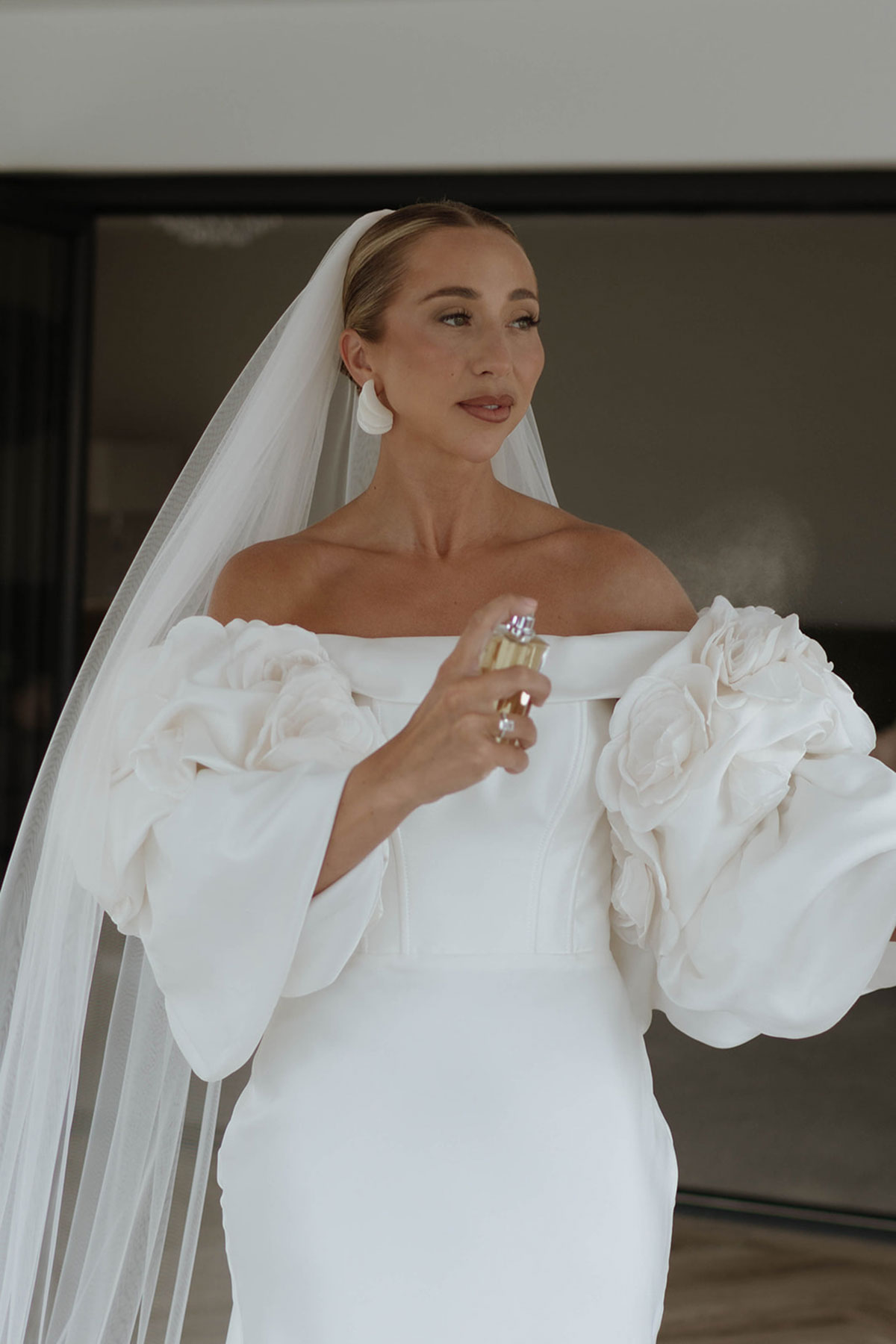 Bride spritzing perfume in off-the-shoulder wedding dress with dramatic floral sleeves before Ayrshire marquee wedding