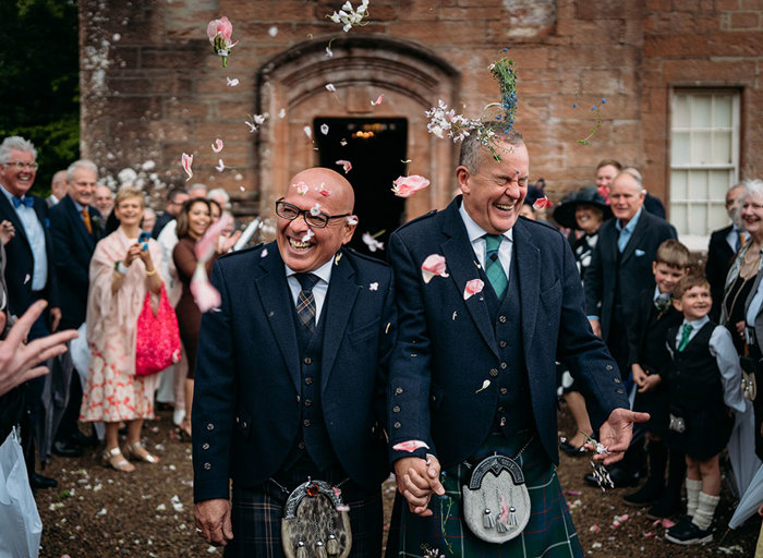 two grooms holding hands being showered in flower petal confetti outside Brodick Castle