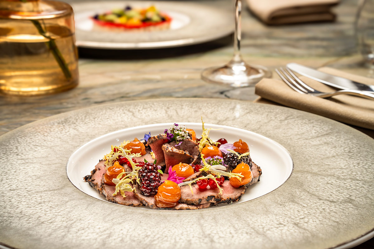 Fine dining dish served aboard Fingal in Edinburgh, featuring venison, vibrant seasonal vegetables and edible flowers on an elegant plate