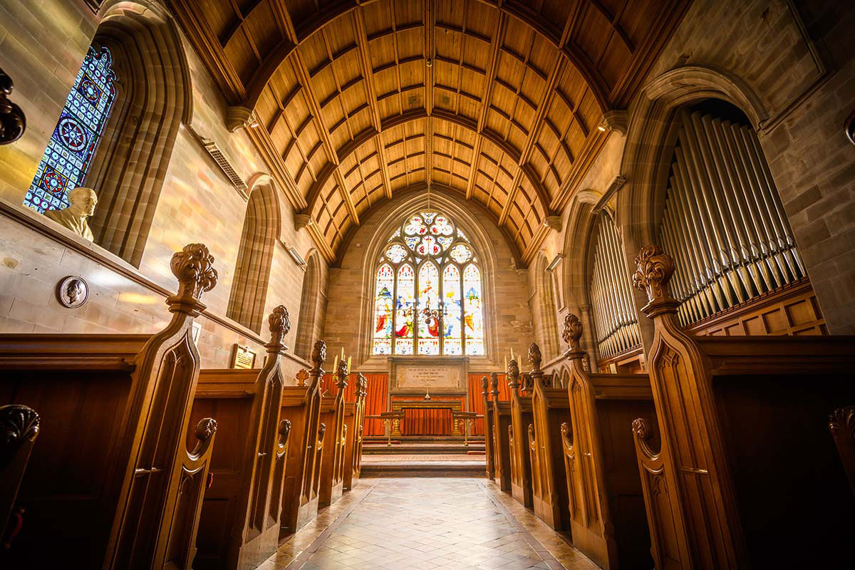 Ornate chapel interior with wooden pews, arched ceiling, organ pipes, and stained-glass windows above the altar