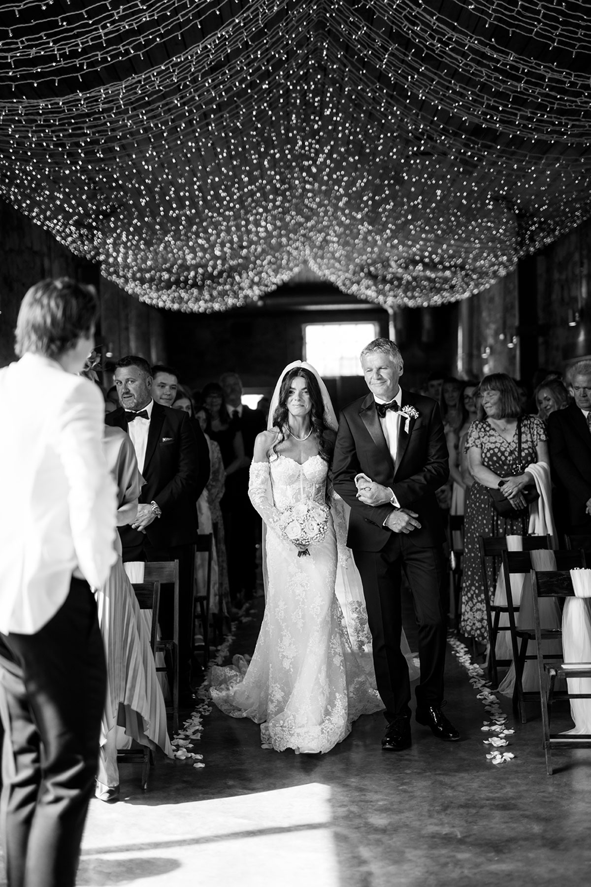 Bride walking down the aisle with her dad under fairy lights at a rustic Scottish wedding venue