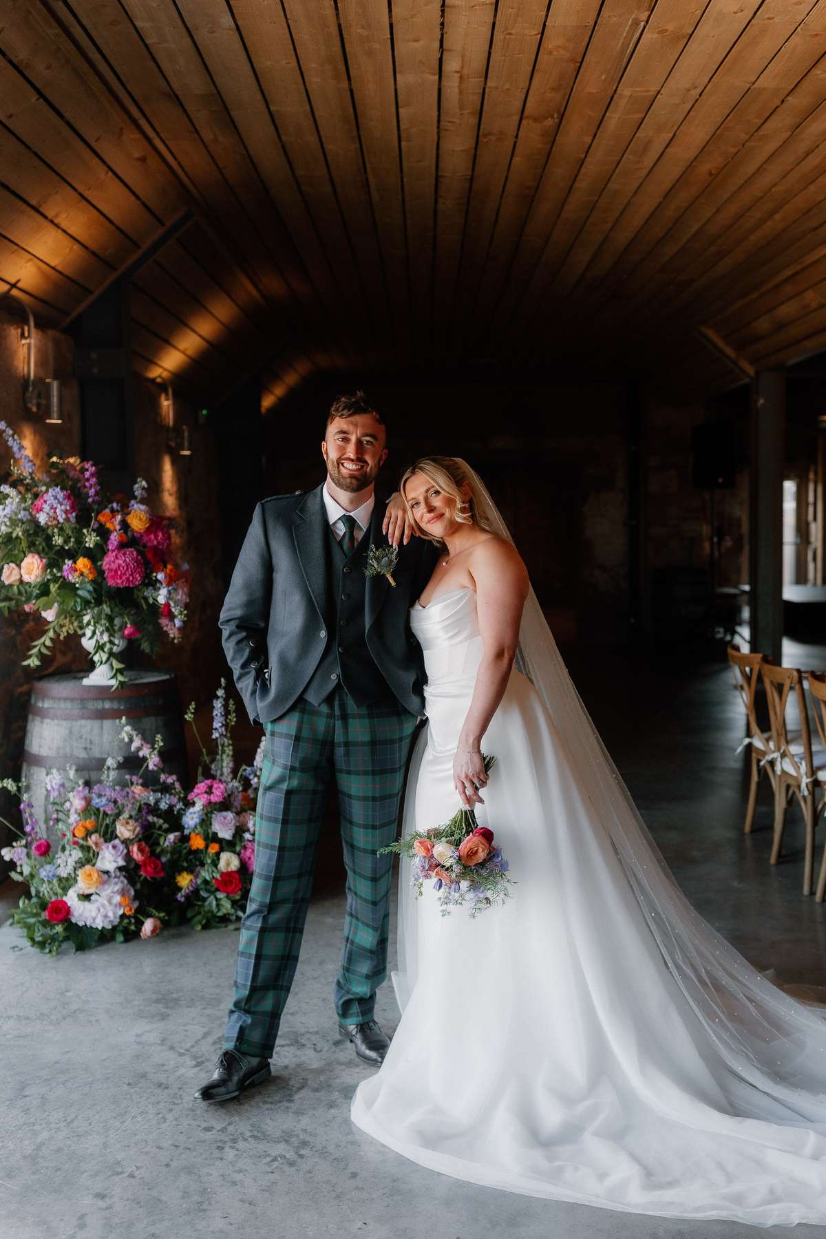 Relaxed bride and groom portrait inside Falside Mill wedding venue surrounded by colourful floral displays