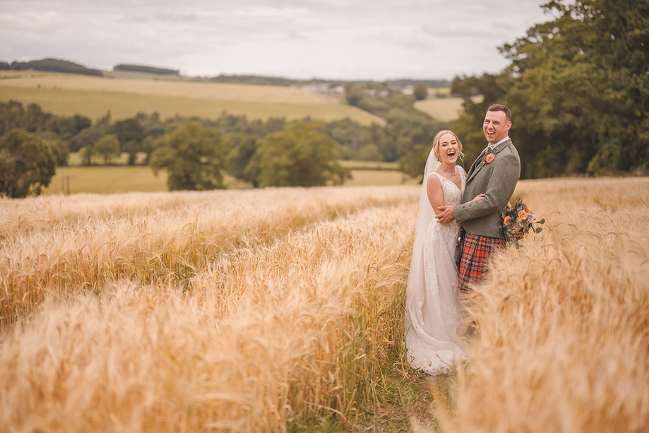 A bride and groom stand close together in a wheat field