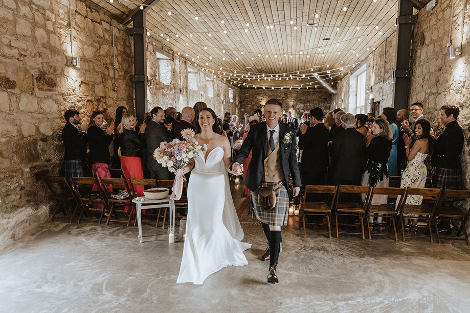 bride and groom leave wedding ceremony as guests cheer