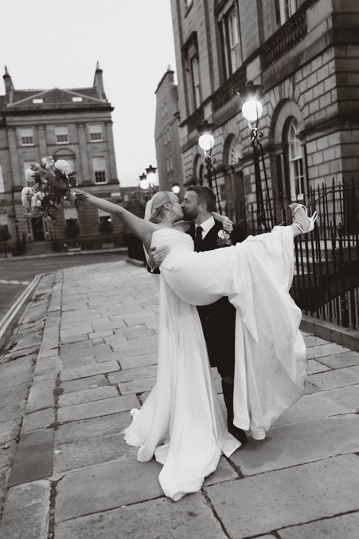 black and white photo of groom lifting bride on Edinburgh street outside historic building