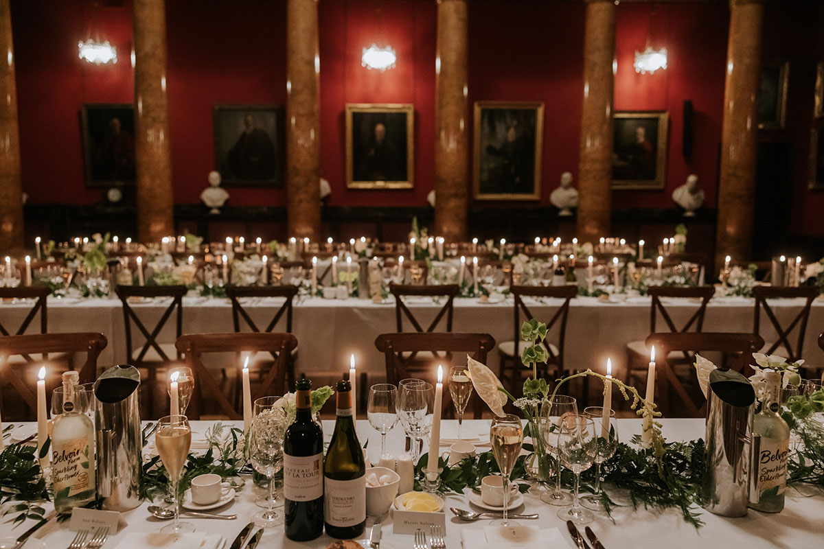 Elegant wedding banquet with candles, wine bottles, and greenery table arrangements.