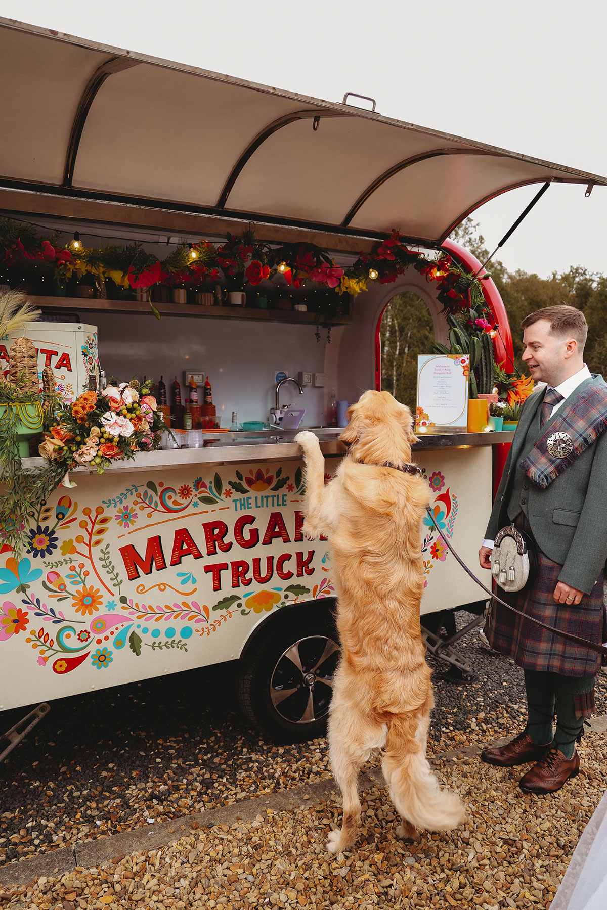 Golden retriever standing at a colourful margarita truck with the groom during a Scottish wedding reception