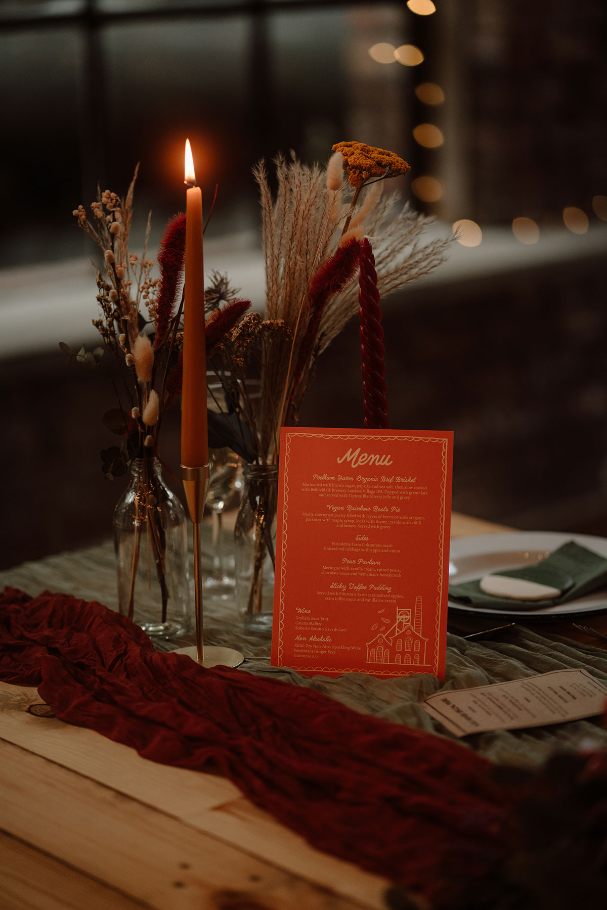 Autumn-inspired wedding table styling with dried flowers, taper candles, coloured menu card and rich red fabric runner at a Scottish wedding reception