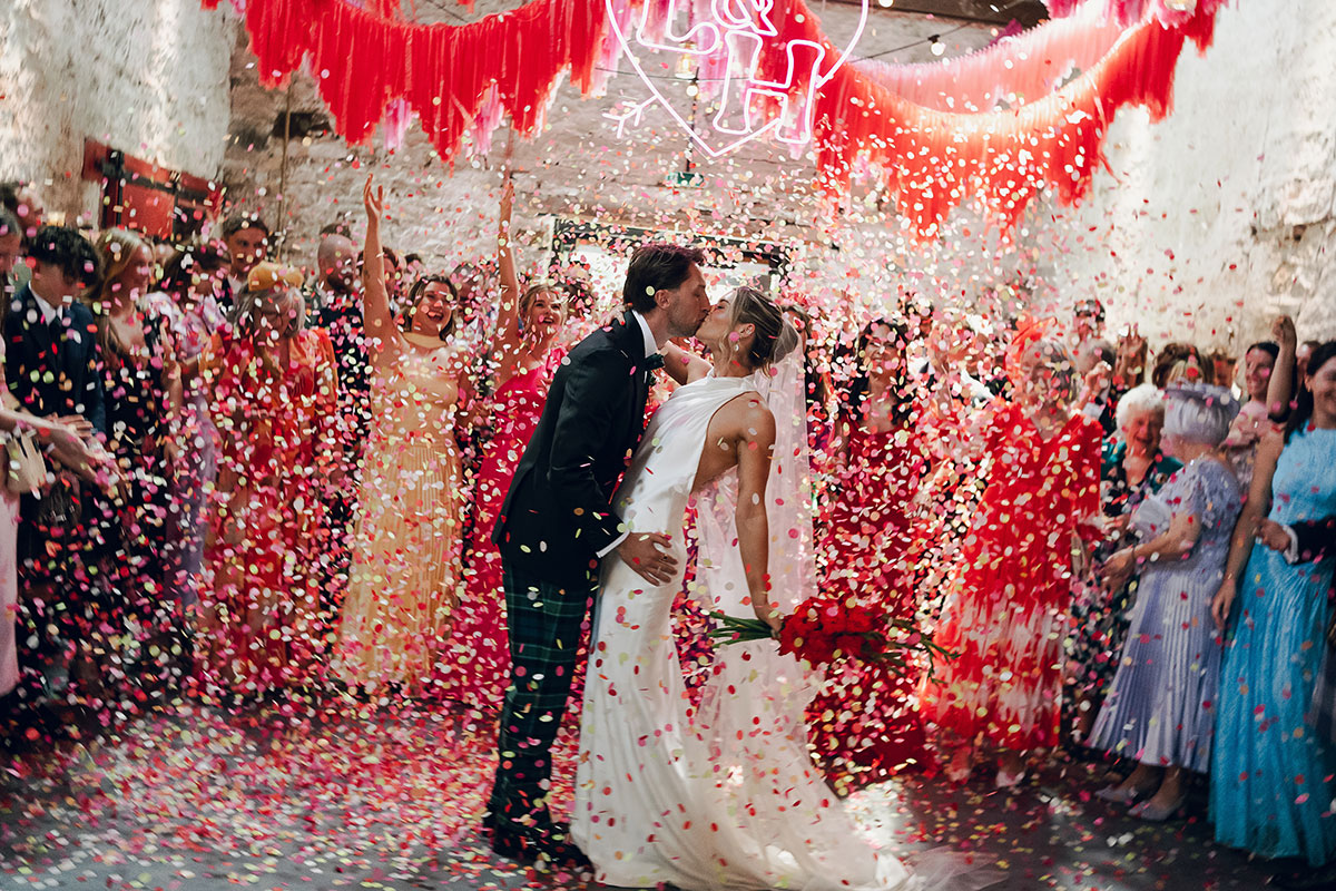 Bride and groom celebrate beneath a dramatic confetti cannon explosion surrounded by guests and colourful Mexican-inspired wedding décor at Kinkell Byre.