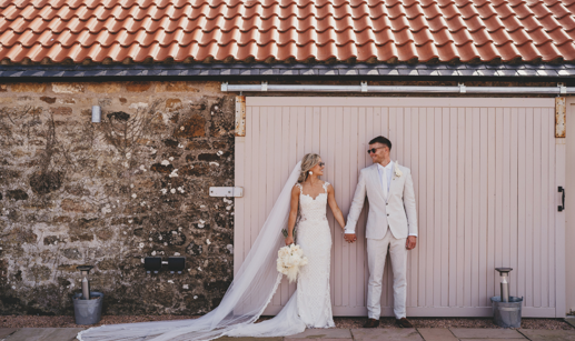 Bride and groom standing outside holding hands and wearing sunglasses