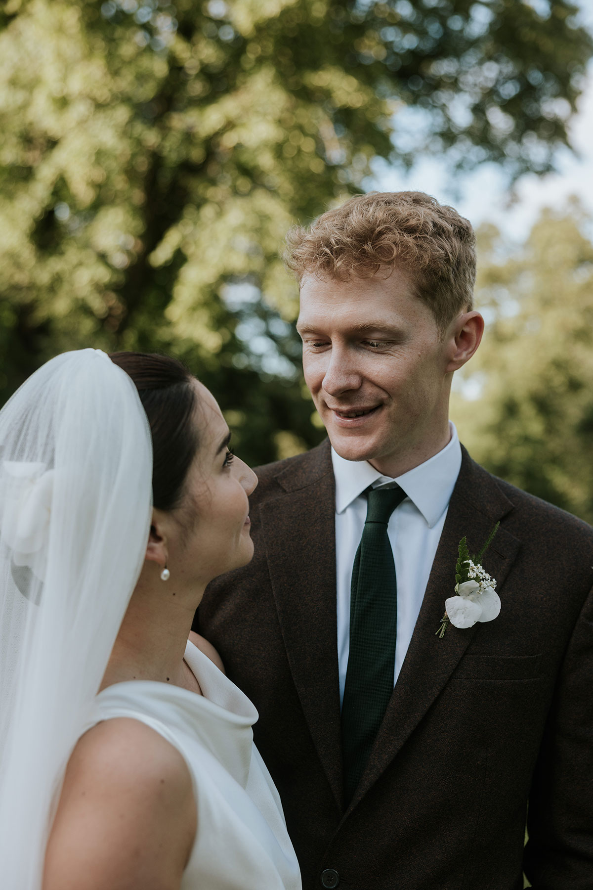 Close-up of bride and groom smiling at each other outdoors on wedding day.