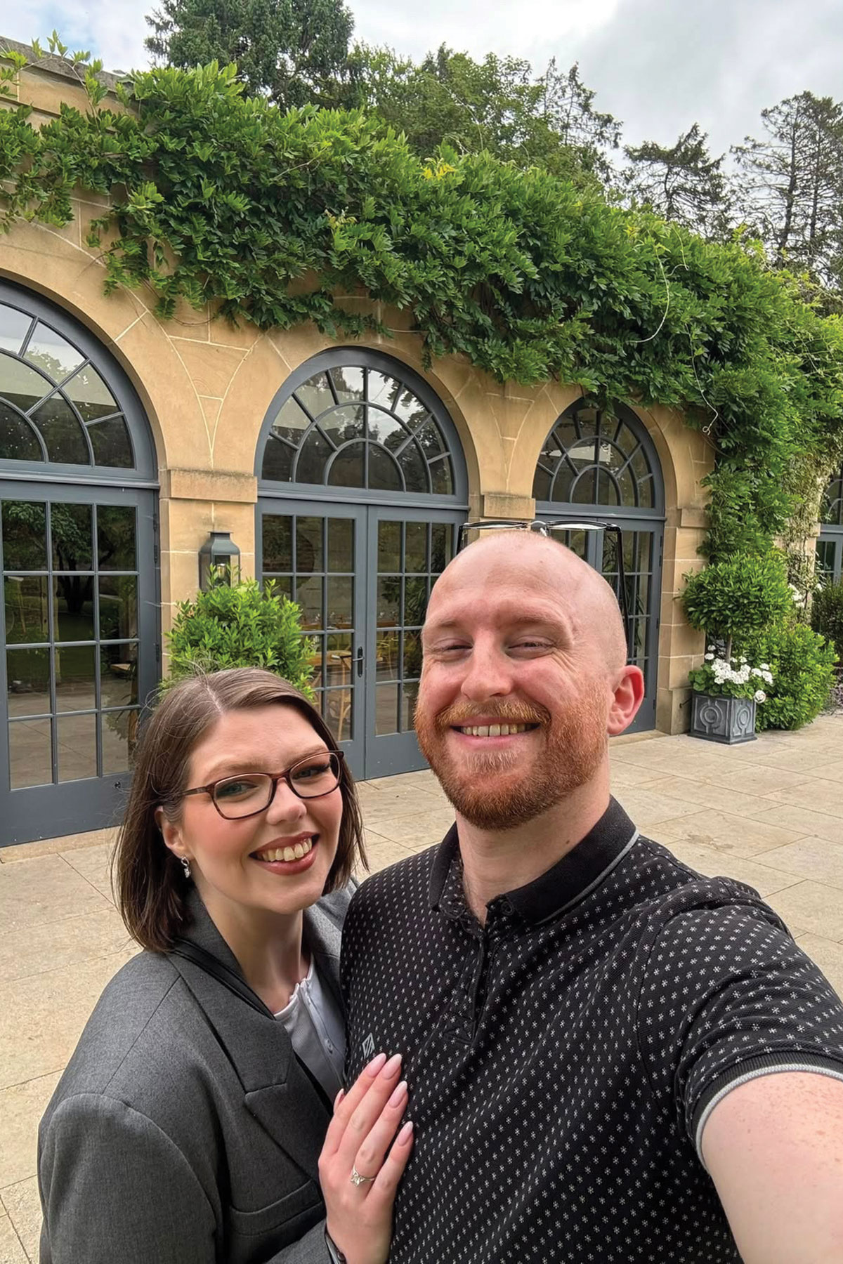 Couple taking a selfie outside a luxury country house wedding venue with elegant stone architecture and landscaped gardens