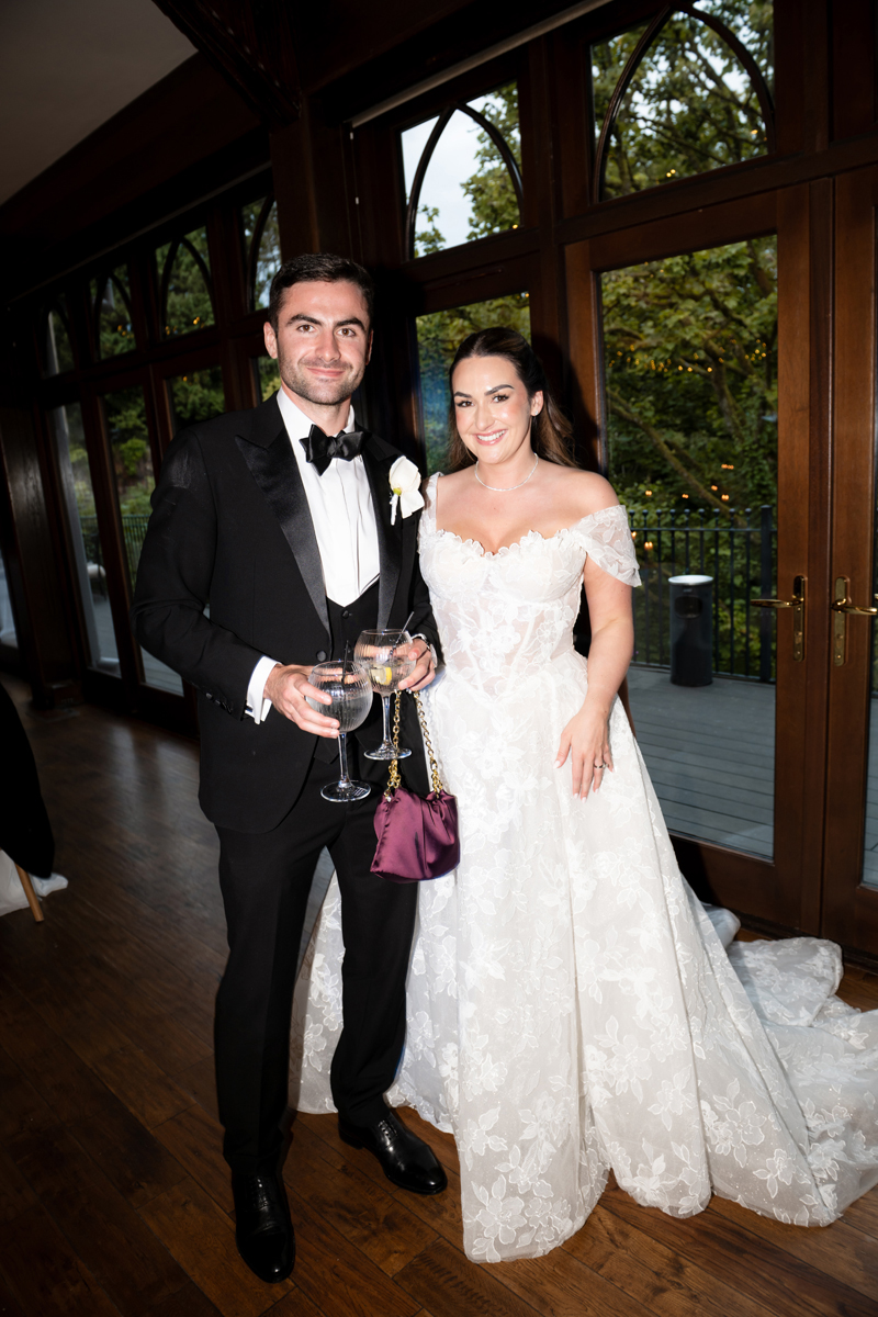 Bride in an off-the-shoulder lace wedding dress posing with a guest in black tie at Crossbasket Castle.