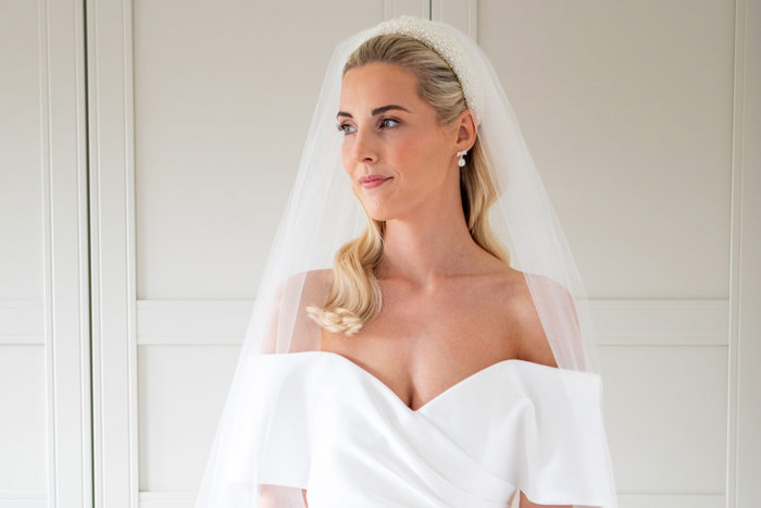 a blonde bride wears a pearl headband and veil, smiling and looking to the side