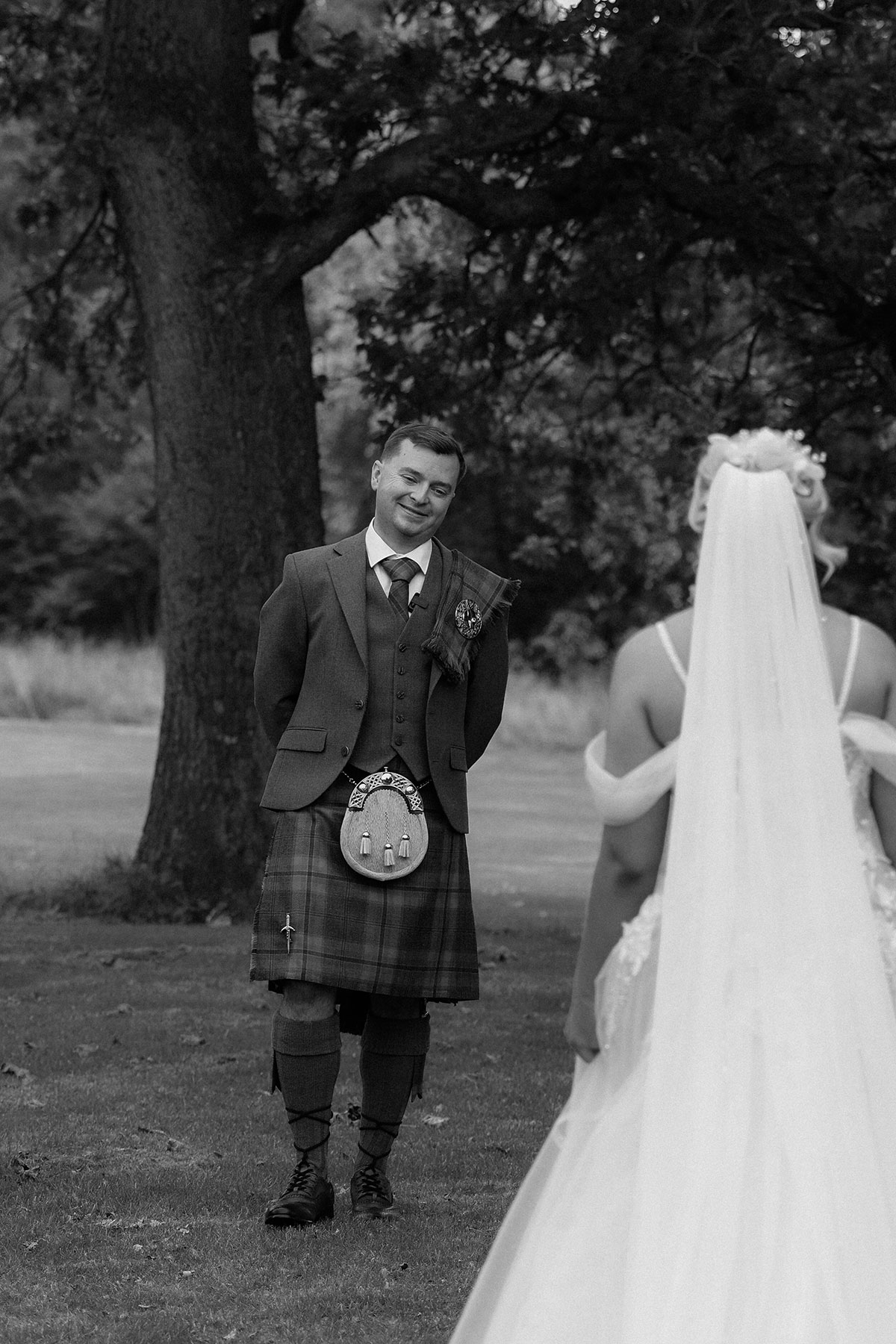Groom smiling during an emotional first look as the bride approaches in a woodland setting at a Scottish wedding