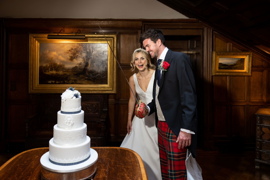 Couple cut four-tier white cake with a sword