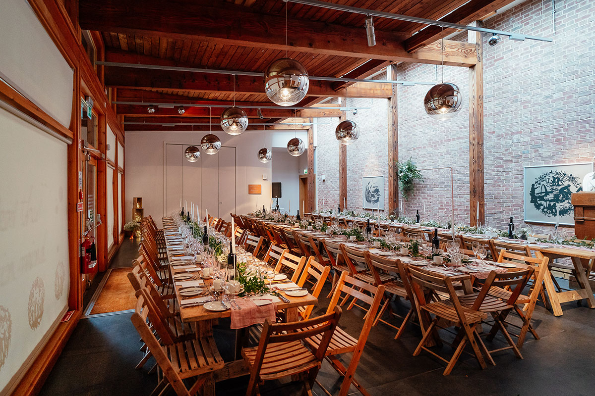 The Robertson Room at the Robert Burns Birthplace Museum set for a wedding meal, with long wooden tables, folding chairs and modern pendant lights.