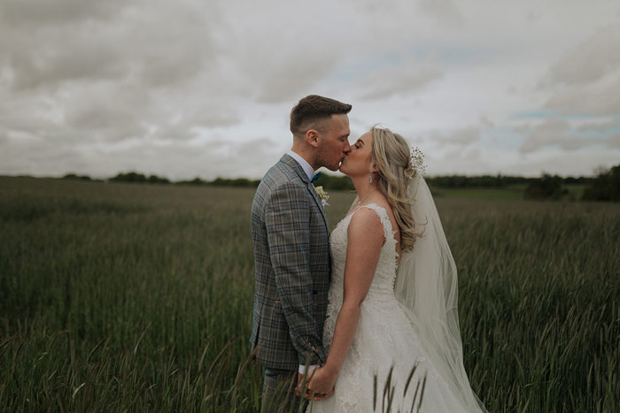 A Bride And Groom Kiss While Standing In A Field Of Tall Grass