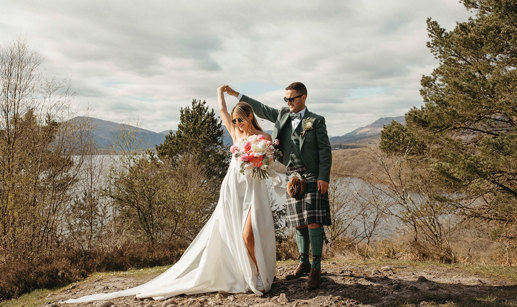 A Bride And Groom Dancing on a stony surface with trees, a lake and countryside in the background