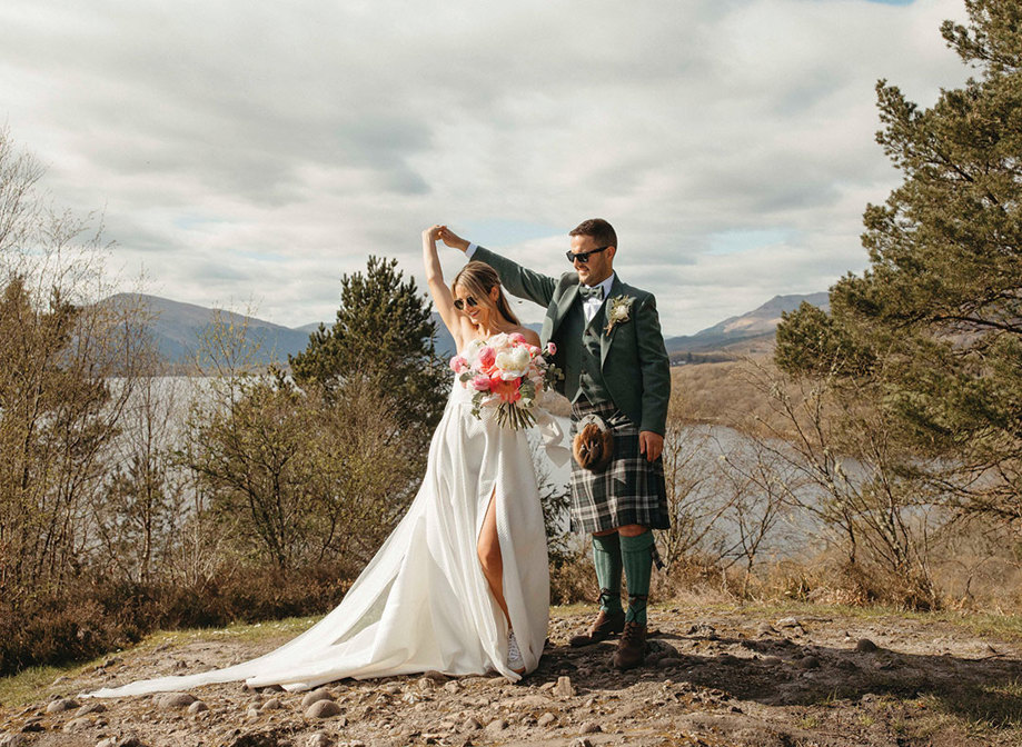 A Bride And Groom Dancing on a stony surface with trees, a lake and countryside in the background