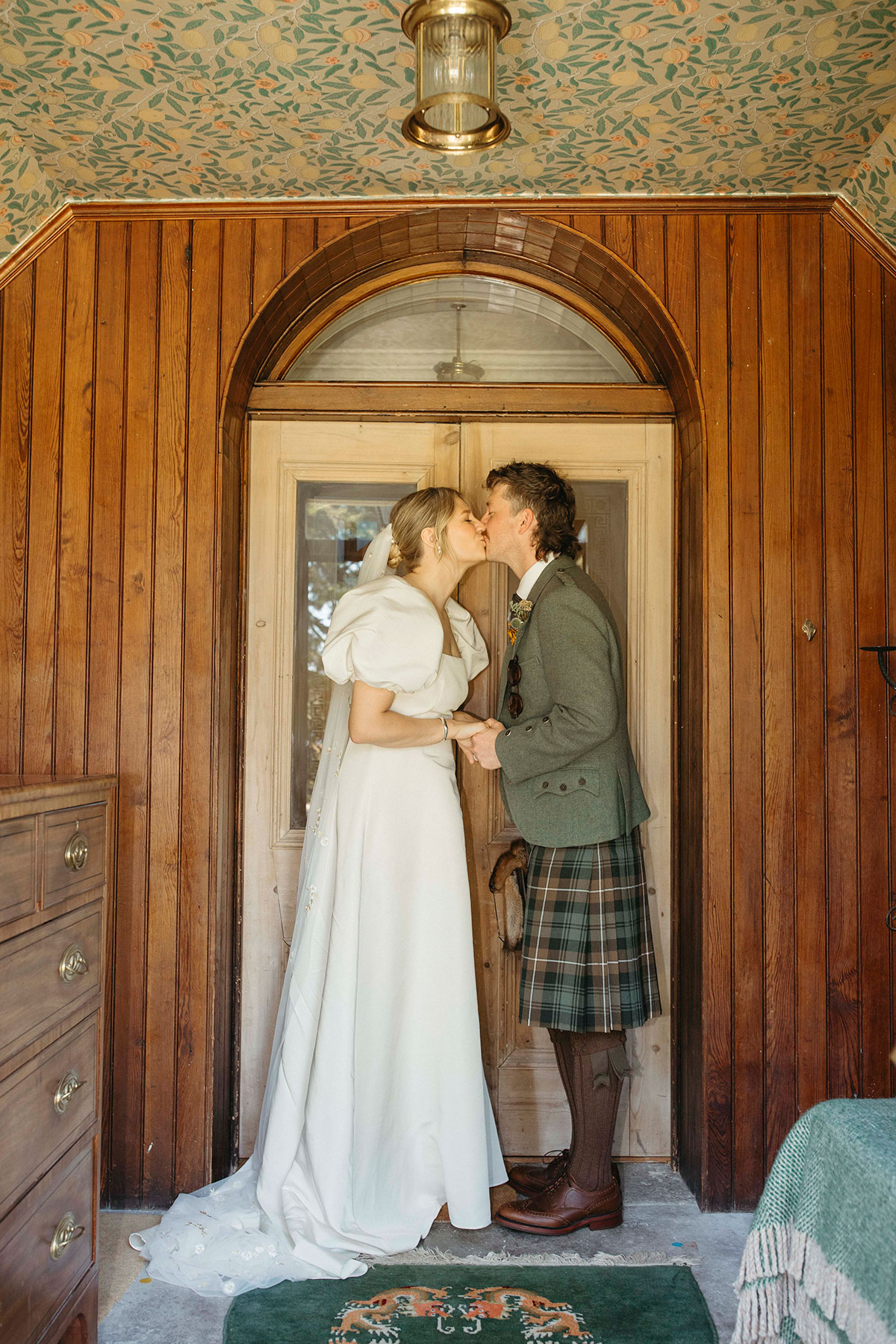 Bride and groom share a kiss inside Georgian Highland farmhouse during Nethy Bridge wedding