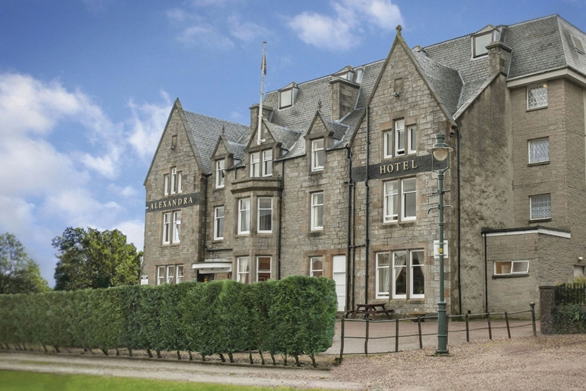the exterior of a large grey brick building that says 'Alexandra Hotel' across the front on a day with blue skies
