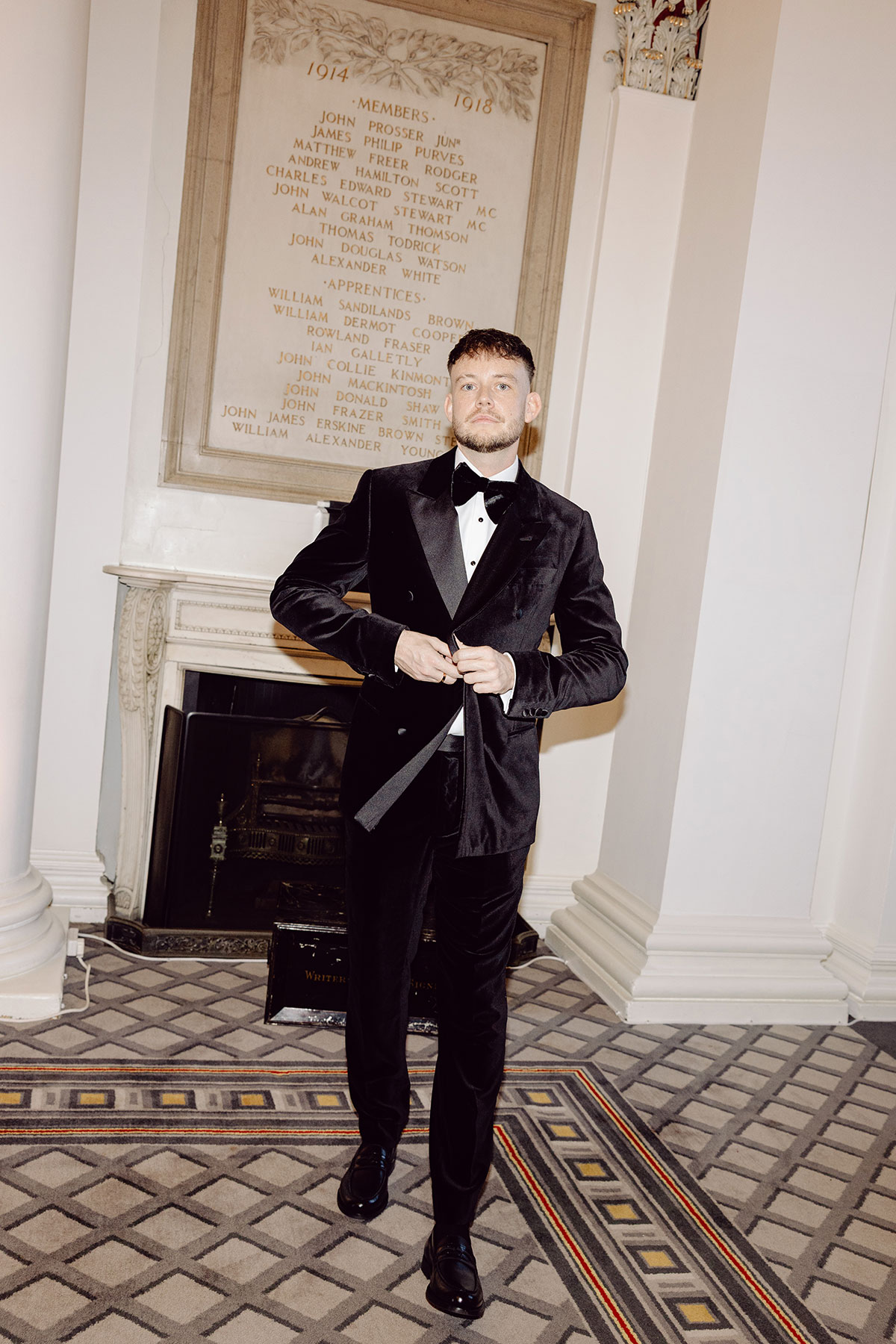 Groom in a black velvet tuxedo adjusting his jacket inside The Signet Library