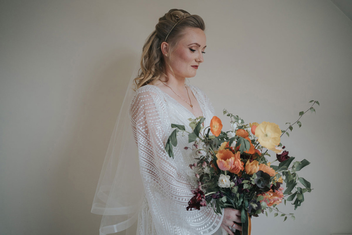Bride smiles as she looks down at bouquet filled with orange flowers 