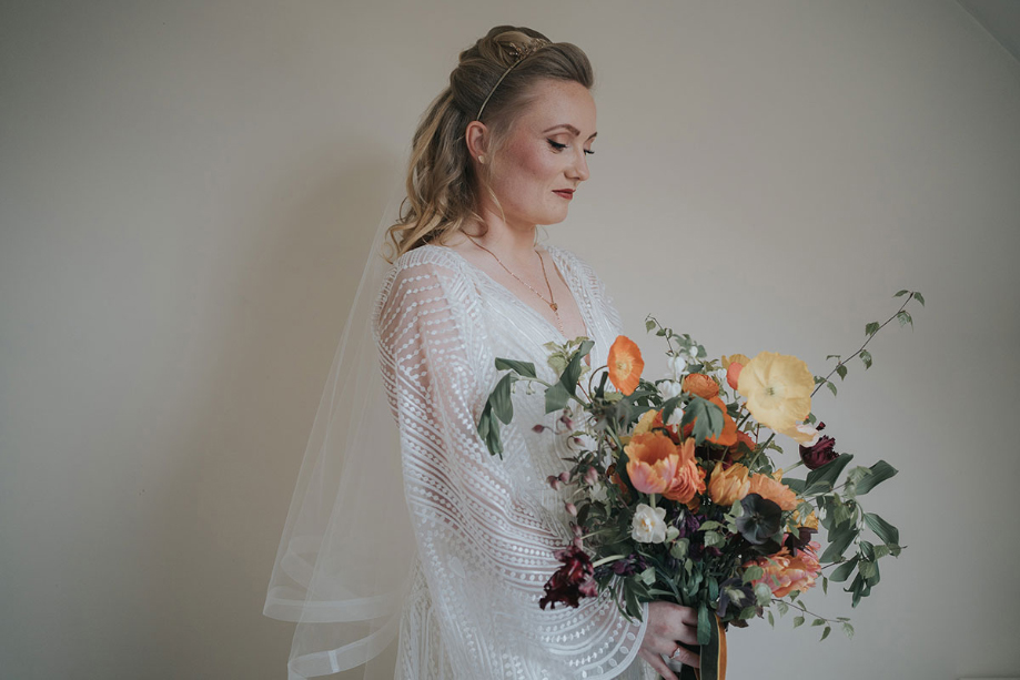Bride smiles as she looks down at bouquet filled with orange flowers