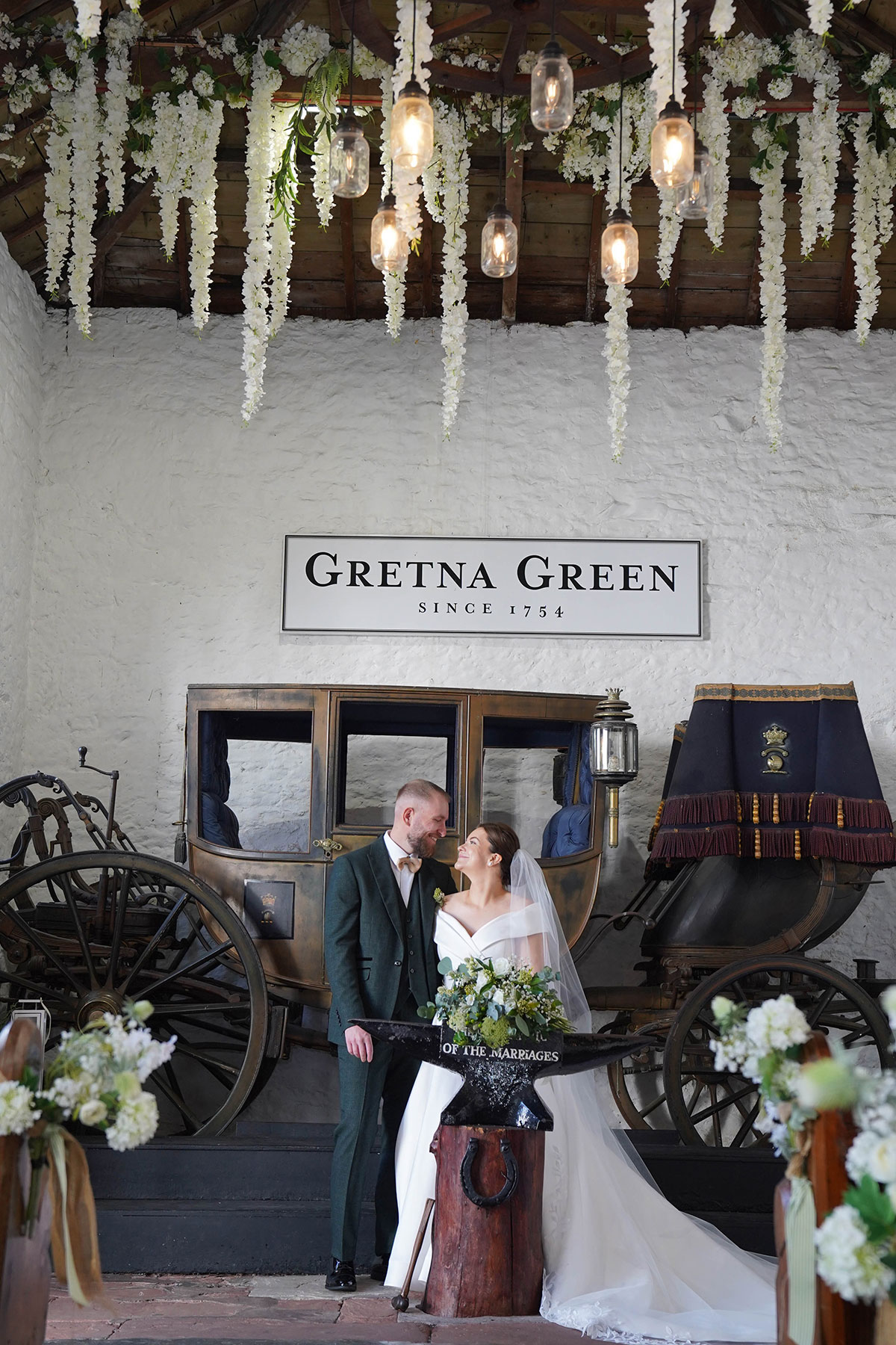 Bride and groom posing beside the marriage anvil inside the Coach House ceremony room at Gretna Hall, Gretna Green.