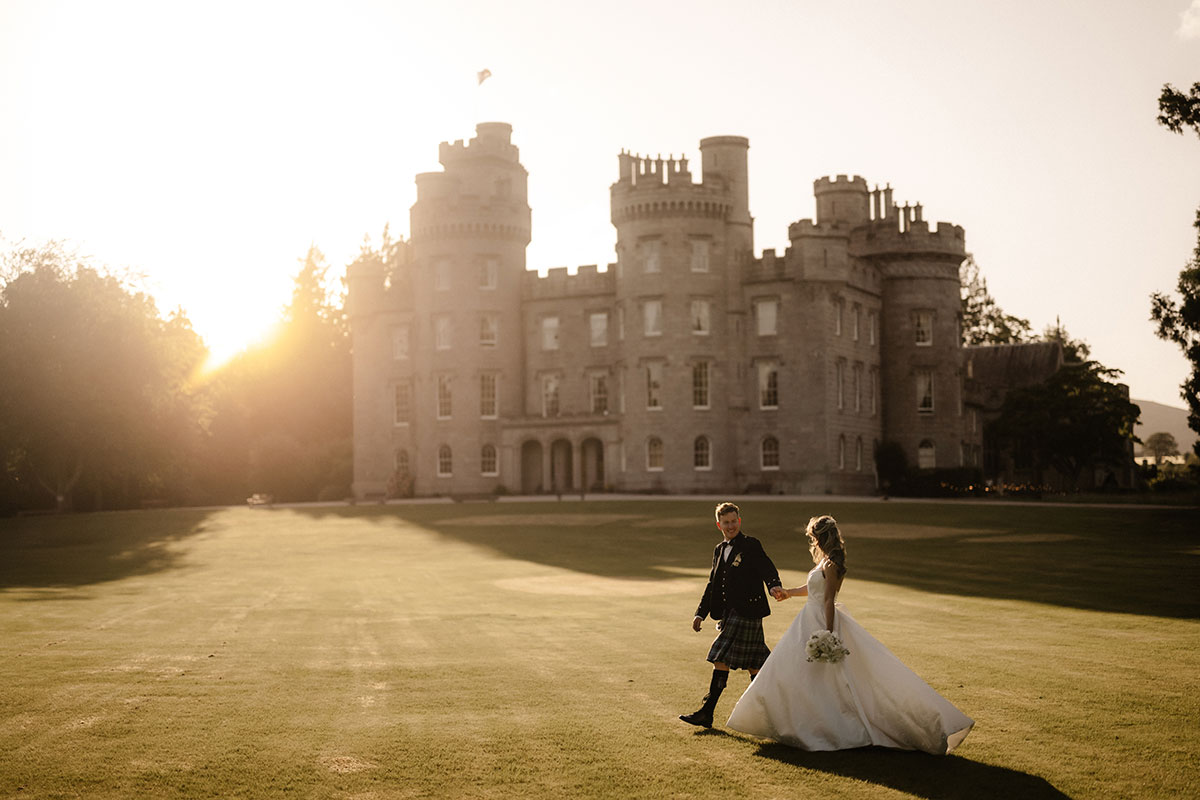 Bride and groom walking across the lawns of Cluny Castle at golden hour, with the historic Scottish castle creating a dramatic backdrop for their Aberdeenshire wedding