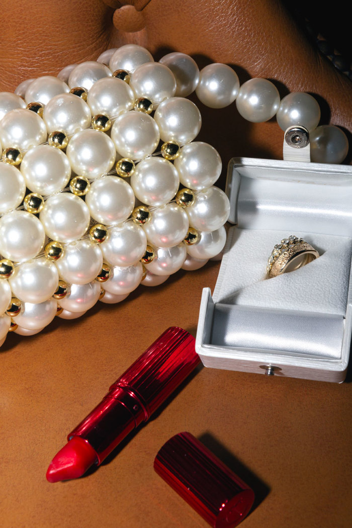 A close up photo of a bag made from large pearls sitting next to an open red lipstick tube and a box with two rings inside