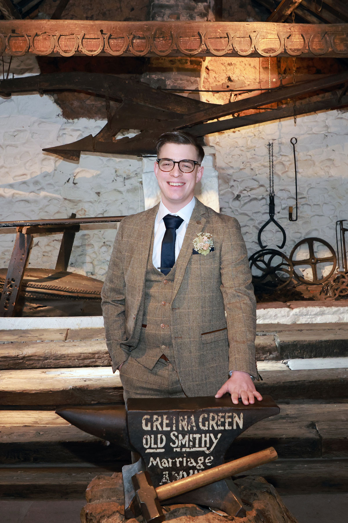 groom smiles for a photograph wearing a brown tweed suit