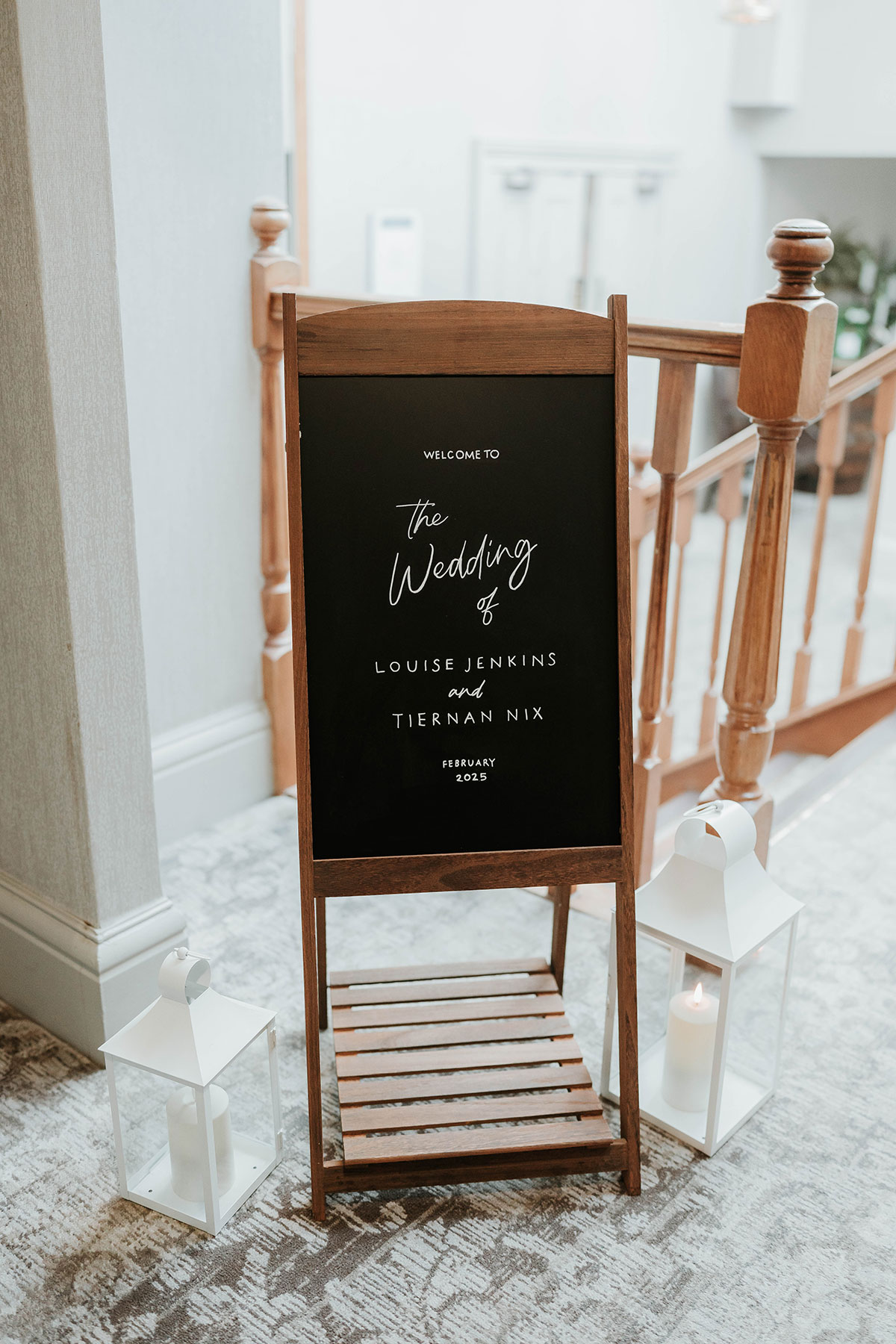 Black wedding welcome sign with white lettering for Louise Jenkins and Tiernan Nix, styled with lanterns